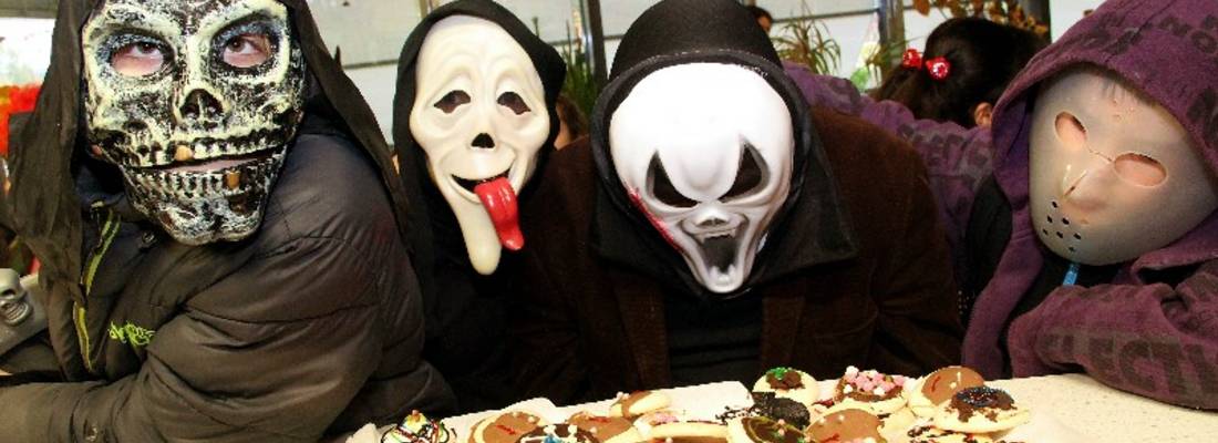 Vier Kinder verkleidet mit Halloweenmasken, im Vordergrund steht ein Tablet mit verzierten Keksen