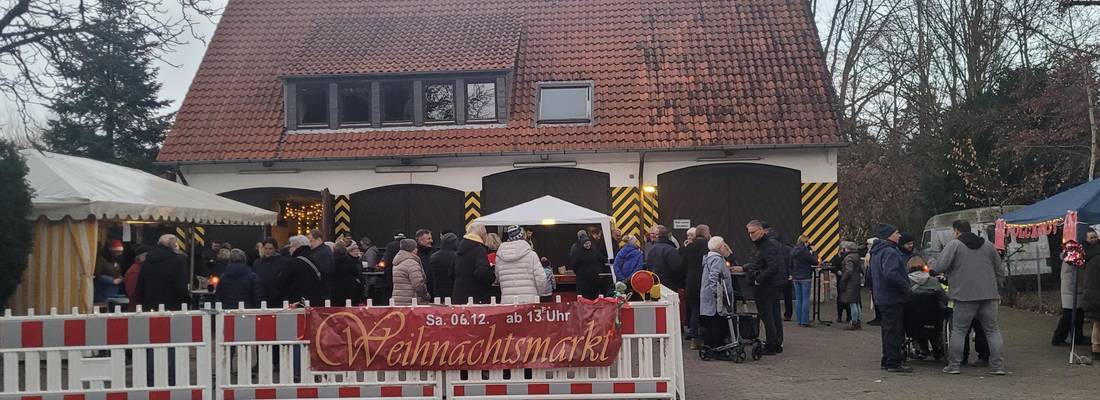 Blick auf das Gelände der alten Feuerwache Gleidingen. Im Vordergrund sind Menschen und Stände hinter einer Absperrung mit dem Banner "Weihnachtsmarkt" zu sehen. Im Hintergrund befindet sich das Gebäude der alten Feuerwache Gleidingen.