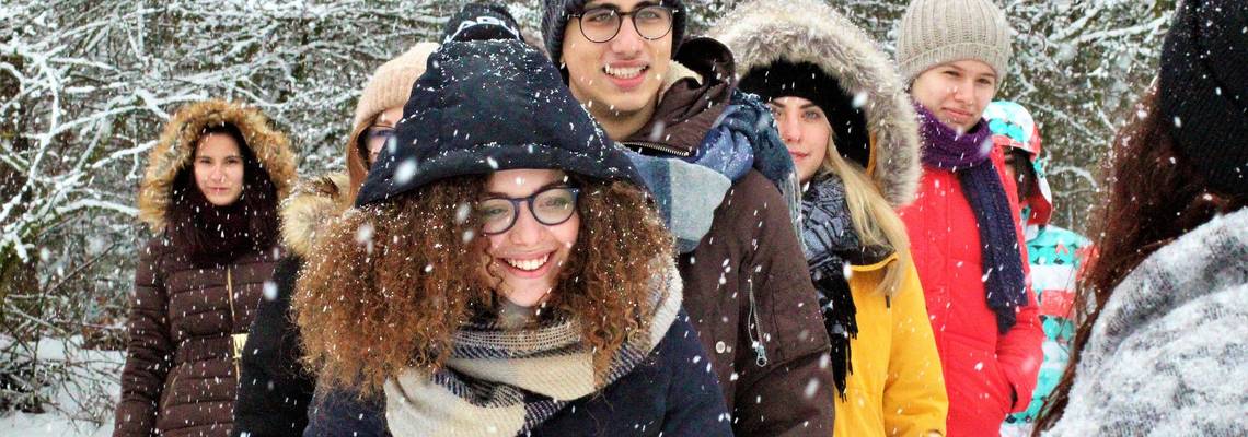 Gruppe von Jugendlichen steht vor Schneebedeckten Bäumen. Es schneit.