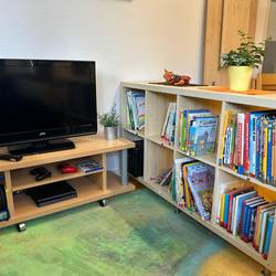 Rollewagen mit TV, daneben ein Sideboard mit Kinderbüchern
