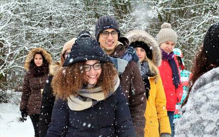 Gruppe von Jugendlichen steht vor Schneebedeckten Bäumen. Es schneit.