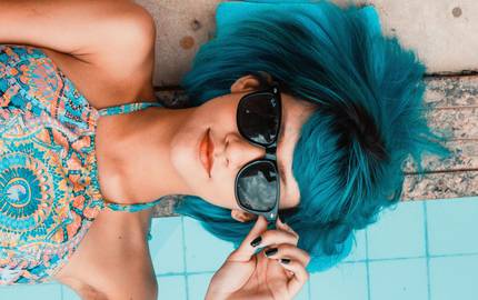 Mädchen mit Sonnenbrille liegt nebem dem Pool