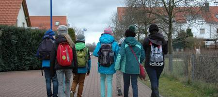 Eine Gruppe von Kindern gehen einen gepflasterten Weg entlang. Die Gruppe ist von hinten zu sehen.