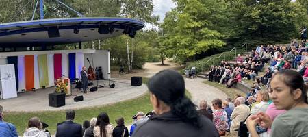 Blick auf die Kulturbühne im Park der Sinne. Bürgermeister Kai Eggert spricht. Viele Personen sitzen im Publikum.