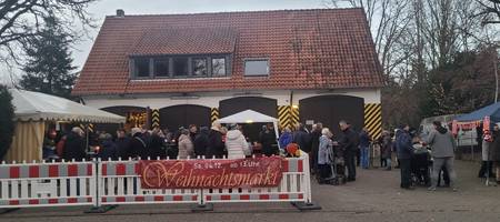 Blick auf das Gelände der alten Feuerwache Gleidingen. Im Vordergrund sind Menschen und Stände hinter einer Absperrung mit dem Banner "Weihnachtsmarkt" zu sehen. Im Hintergrund befindet sich das Gebäude der alten Feuerwache Gleidingen.