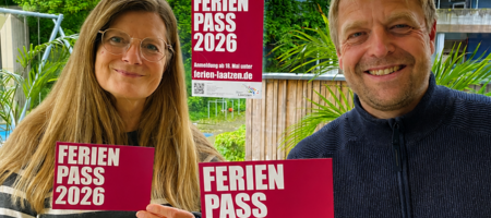 Ein Mann und eine Frau halten die Werbematerialien zum Sommerferienpass in die Kamera.
