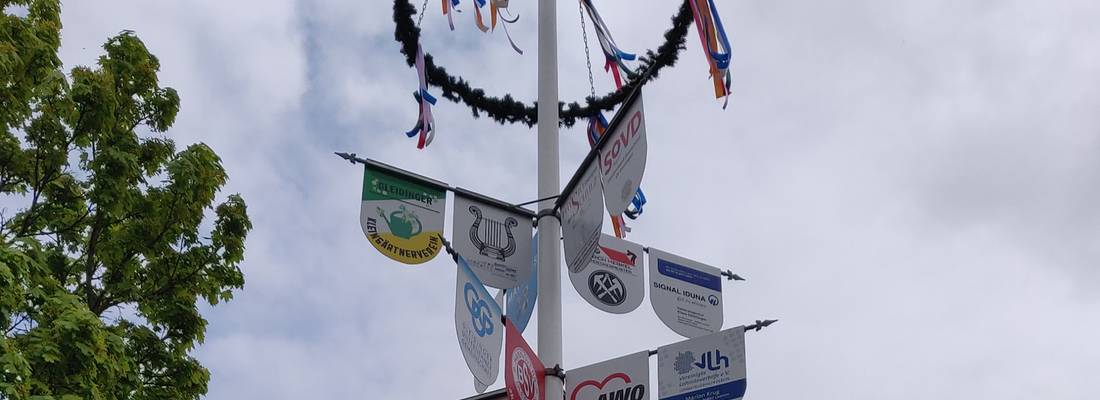 Maibaum mit Schildern verschiedener Unternehmen und Maikranz