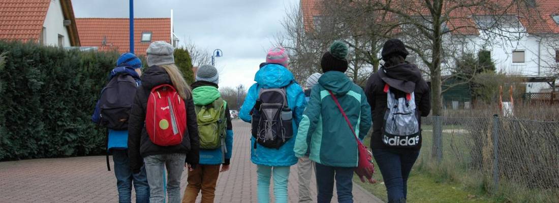 Eine Gruppe von Kindern gehen einen gepflasterten Weg entlang. Die Gruppe ist von hinten zu sehen.