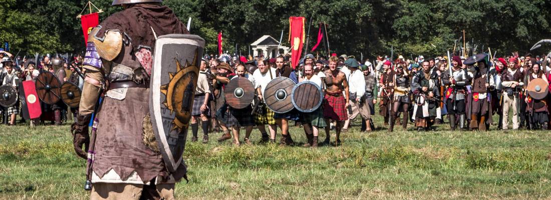Mittelalterlich verkleideter Kämpfer steht mit einem Schild bewaffnet einer Gruppe auf einem Feld gegenüber