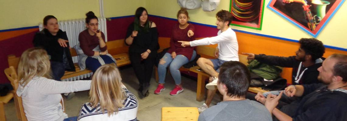 Jugendliche sitzen in einem Kreis und zeigen aufeinander