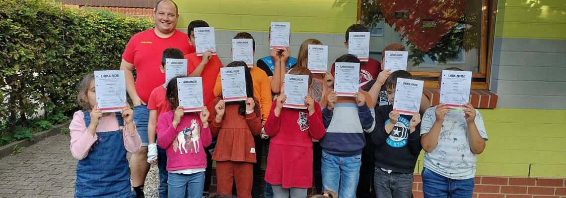 Kinder stehen vor der Quatschkiste mit Urkunden vor dem Gesicht