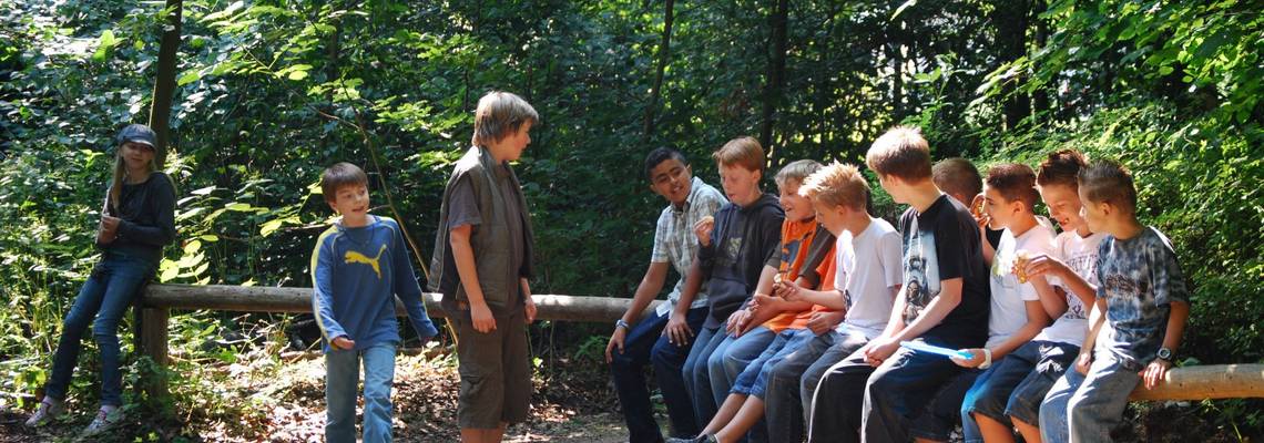 Eine Gruppe Jugendlicher sitzt im Wald auf einem Holzbalken