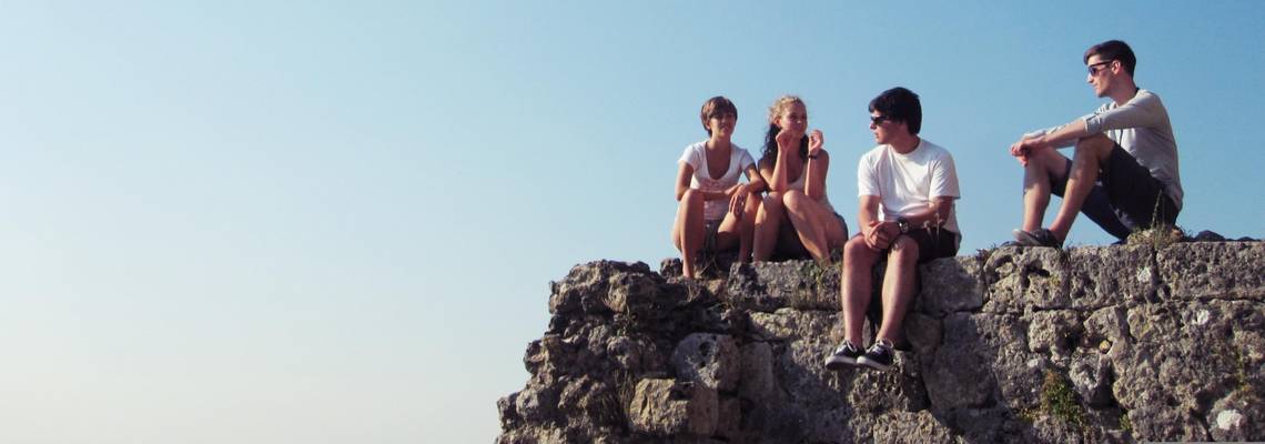Jugendliche auf einem Felsen © pixabay Junge Menschen sitzen in der Natur auf einem Felsen vor blauem Himmel