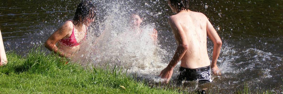 Drei Jugendliche bespritzen sich in einem See mit Wasser ©Pixabay