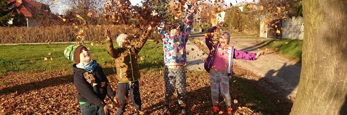 Vier Kinder werfen Laub in die Luft und lachen