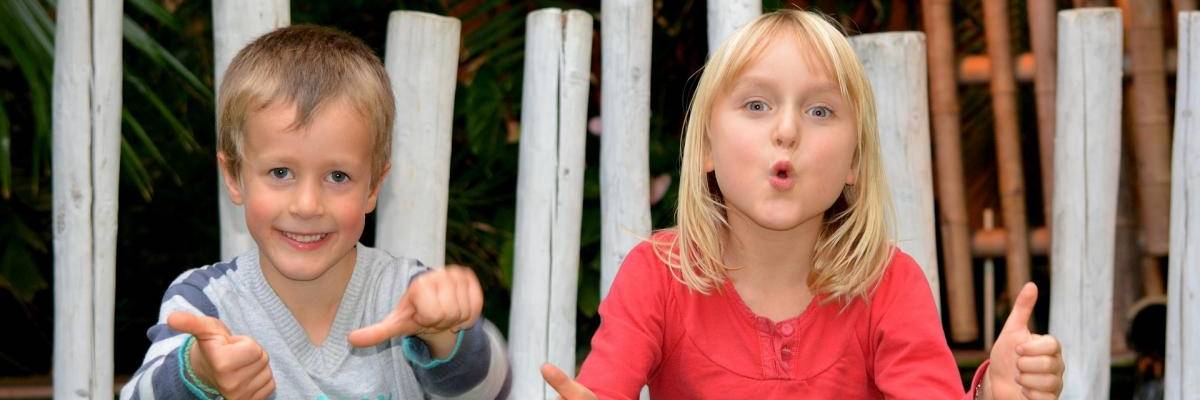 Zwei Kinder sitzen auf einem Stein und zeigen Daumen hoch und Daumen seitwärts