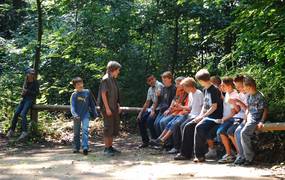 Eine Gruppe Jugendlicher sitzt im Wald auf einem Holzbalken