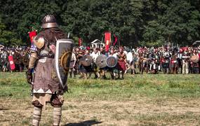 Mittelalterlich verkleideter Kämpfer steht mit einem Schild bewaffnet einer Gruppe auf einem Feld gegenüber