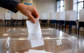 Hand legt Stimmzettel in durchsichtige Wahlurne