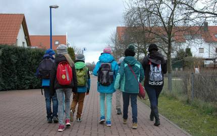 Eine Gruppe von Kindern gehen einen gepflasterten Weg entlang. Die Gruppe ist von hinten zu sehen.