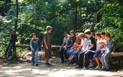 Eine Gruppe Jugendlicher sitzt im Wald auf einem Holzbalken
