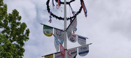 Maibaum mit Schildern verschiedener Unternehmen und Maikranz