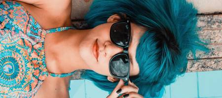 Mädchen mit Sonnenbrille liegt nebem dem Pool