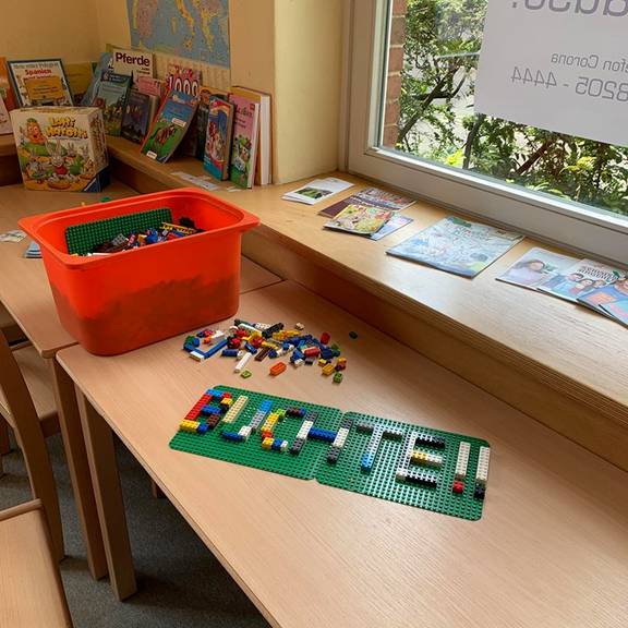 Das Wort "Buchte" liegt aus Lego gebaut auf dem Tisch, im Hintergrund sind Bücher und Spiele
