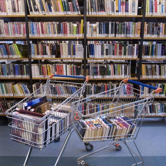 zwei mit Büchern gefüllte Einkaufswagen stehen vor Bücherregalen der Bücherei